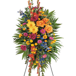 Tall standing spray of bright yellow, orange, pink, and blue flowers on an easel.