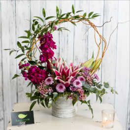 Magenta and pink floral arrangement in a white vase with a decorative twig arch