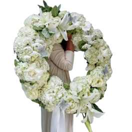 Large white floral wreath with lilies and hydrangeas held by a person