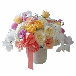 Bouquet of pastel roses and white orchids in a textured vase with a pink ribbon