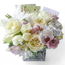 Bouquet of white and blush roses with orchids in a clear square vase