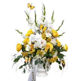 White and yellow floral arrangement in a white vase with butterfly accents