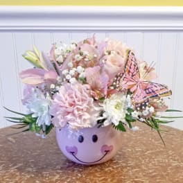 Pastel flower arrangement in a smiley-face ceramic pot with a butterfly accent