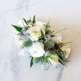 White rose wrist corsage with green accents and silver ribbon coils