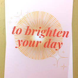 Folded pastel card with coral text 'to brighten your day' over a golden sunburst and small star accents.
