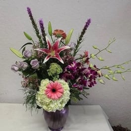 Mixed bouquet with lilies, roses, orchids, and a gerbera in a purple vase
