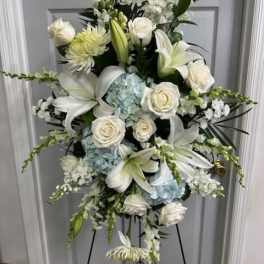 White floral standing spray with lilies, roses, and blue hydrangeas on an easel