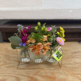 Small mixed flower arrangement in clear glass vases on a gold stand