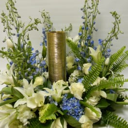 White lilies and blue flowers arranged around a gold cylinder centerpiece