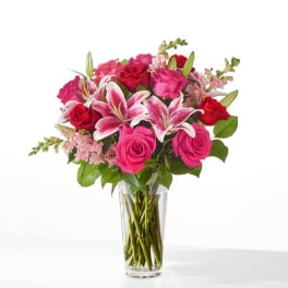 Pink and red roses with lilies in a clear glass vase