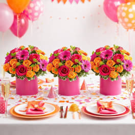Three pink vases hold mixed rose bouquets on a decorated party table.