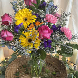 Bouquet of pink roses, yellow gerbera daisies, and purple flowers in a glass vase