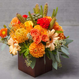 Orange and peach floral arrangement in a square wooden vase