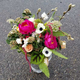 Mixed arrangement of hot pink blooms, white anemones, and peach roses in a clear glass vase