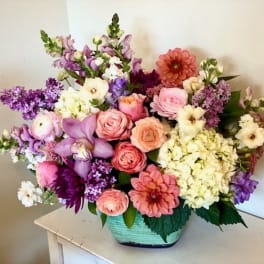 Mixed bouquet of pink, purple, and cream flowers in a green basket