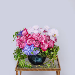 Pink roses and white orchids in a dark vase with trailing greenery