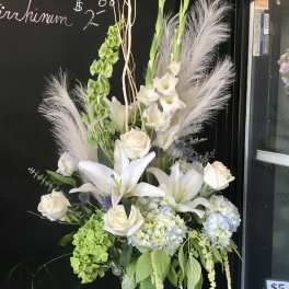Tall white floral arrangement in a glass vase with lilies, roses, and hydrangeas