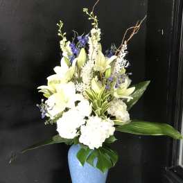 White lilies and blue flowers arranged in a blue vase