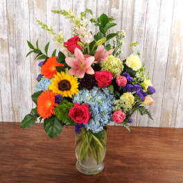 Tall mixed flower arrangement with lilies, roses, sunflowers, gerbera daisies and hydrangeas in a clear vase