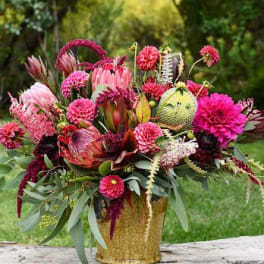 Bright pink and burgundy floral arrangement in a gold vase