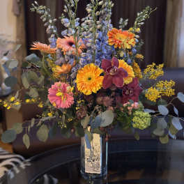 Mixed bouquet in a glass vase with orange, pink, purple, and yellow blooms