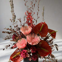 Tall floral arrangement with red anthuriums and pink protea in a black vase