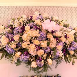 Large pastel floral spray with roses, hydrangeas, and a pink ribbon