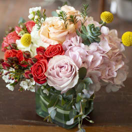 Mixed bouquet of roses, hydrangeas, and succulents in a green glass vase