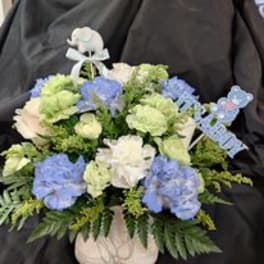Blue and white floral arrangement in a white vase with ribbon picks