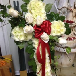 White floral cross arrangement with a red ribbon and roses