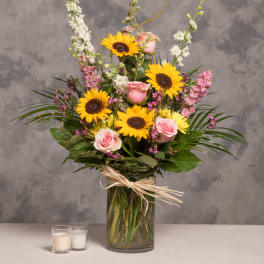 Bouquet of sunflowers and pink roses in a glass vase with candles nearby