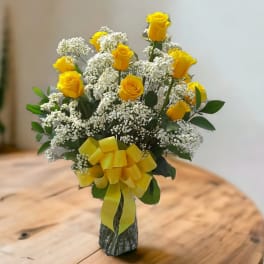 Yellow roses with white baby's breath in a glass vase tied with a yellow ribbon.