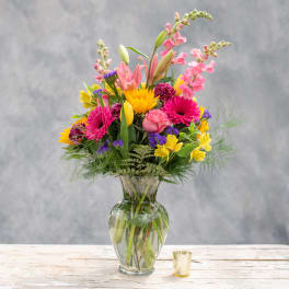 Mixed bouquet of pink, yellow, and purple flowers in a clear glass vase