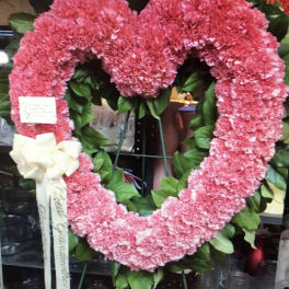 Pink heart-shaped floral wreath on an easel with a white ribbon bow