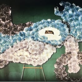 Floral funeral wreaths in blue, white, and black on stands