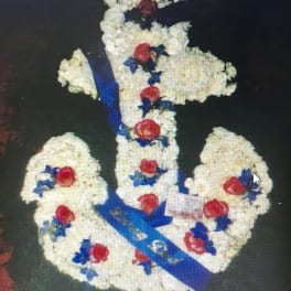 Floral arrangement shaped like a cross with white flowers, red roses, and blue ribbon