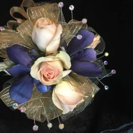 Corsage with pale roses, purple petals, and gold ribbon on black fabric