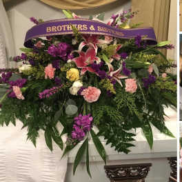 Large funeral spray with lilies, roses, and carnations under a purple ribbon