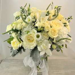 Cream and white floral bouquet in a clear vase with a sheer ribbon