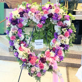 Heart-shaped floral wreath with pink, purple, and white flowers on a stand