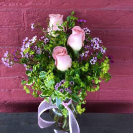 Pink roses in a glass vase with purple filler flowers and a ribbon