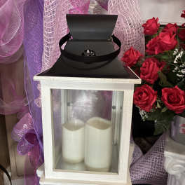 White lantern with two pillar candles beside red roses