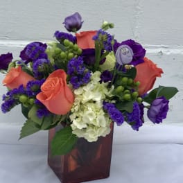 Colorful bouquet of roses, hydrangea, and purple filler in a square vase