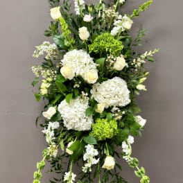Tall standing spray of white roses and hydrangeas with green accents on an easel stand