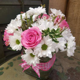 Pink roses and white daisies in a glass vase with a pink ribbon