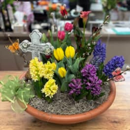 Mixed spring flowers in a shallow terracotta bowl with a decorative cross