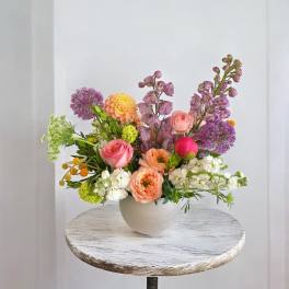Mixed bouquet in a round white vase with pink, purple, peach, and white flowers