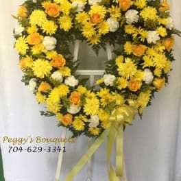 Heart-shaped yellow and white floral wreath on a stand with ribbon