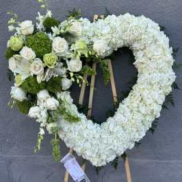 Heart-shaped floral wreath with white flowers and green accents on an easel