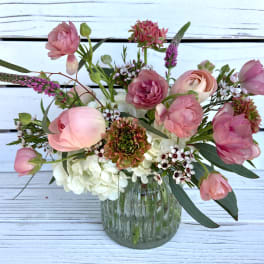 Small glass vase with pink ranunculus and mixed flowers in a loose, airy arrangement